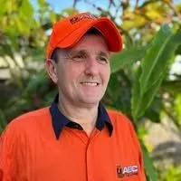 Man in orange uniform and cap with ABC Test Tag and Fire logo, smiling outdoors, emphasizing professional electrical safety services.